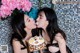 A couple of women kissing each other in front of a cake.