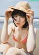 A woman in a bikini and hat sitting on the beach.