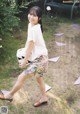 A woman in a white shirt and floral shorts is walking in the grass.